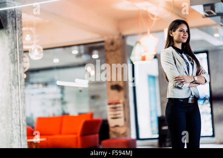 Confident businesswoman standing in office avec les mains croisées Banque D'Images