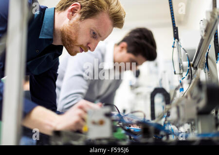 Deux beaux jeunes ingénieurs travaillant sur des composants électroniques et puces cassées de fixation Banque D'Images