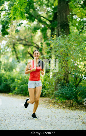 Belle jeune jogger en parc d'écouter de la musique via des écouteurs lors de l'exécution Banque D'Images