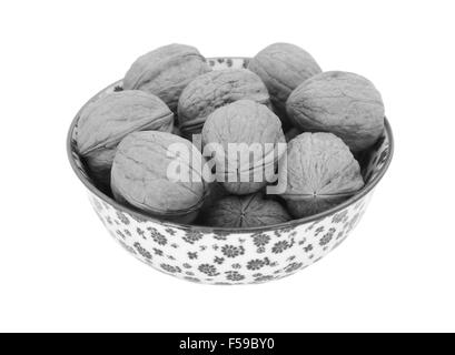 Les noix en coque, dans un bol en porcelaine avec un motif fleuri, isolé sur fond blanc - traitement monochrome Banque D'Images