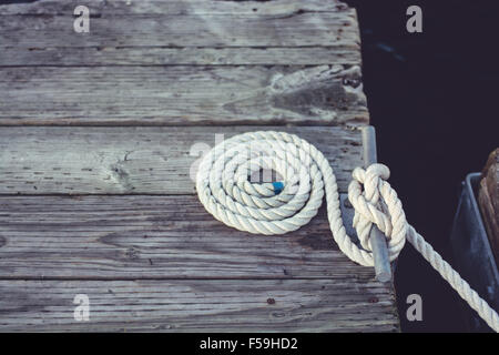 Corde nautique parfaitement enroulé et enroulé sur un vieux quai altérés. Banque D'Images