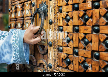Une main tenant une poignée de porte en bois, d'une traditionnelle marocaine, porte, dans le sud du Maroc. Banque D'Images