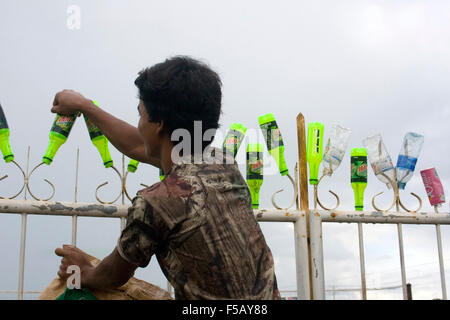 Un homme met les bouteilles en plastique sur une clôture pour recyclage mis à Skun, au Cambodge. Banque D'Images