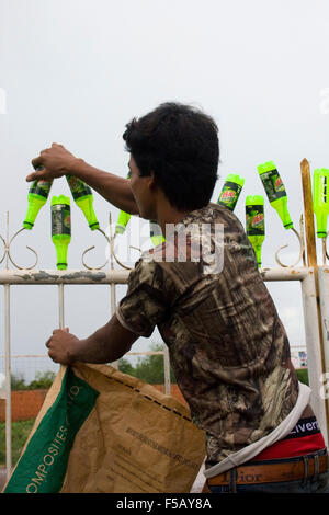 Un homme met les bouteilles en plastique sur une clôture pour recyclage mis à Skun, au Cambodge. Banque D'Images