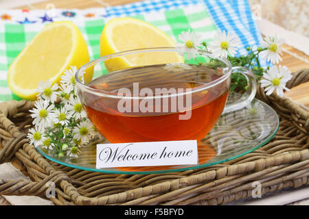 Bienvenue accueil carte avec tasse de thé, de fleurs de camomille et de citron sur le plateau en osier Banque D'Images