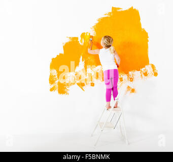 Petite fille peinture mur blanc avec la couleur orange Banque D'Images
