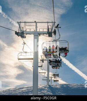 Les skieurs en télésiège avec le coucher du soleil sur une montagne enneigée Banque D'Images