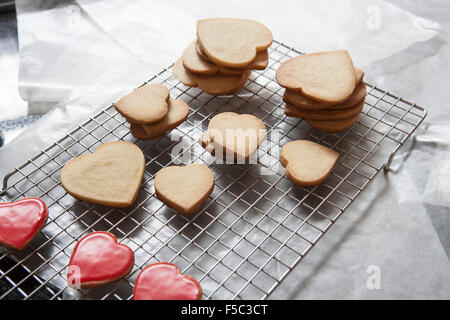 Petits et grands Sablés Heart-Shaped sur grille de refroidissement, certaines avec glaçure rouge Banque D'Images