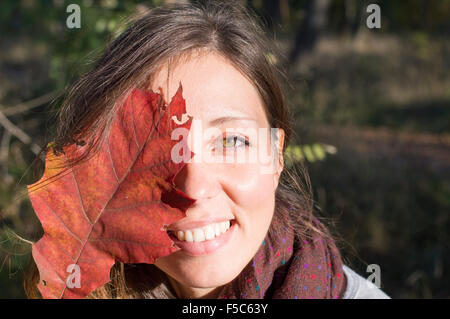 Portrait de beauté d'automne à l'extérieur. Fille avec de magnifiques yeux verts holding red autumn leaf sur son visage dans le parc Banque D'Images