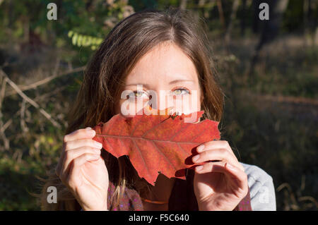 Portrait de beauté d'automne à l'extérieur. Fille avec de magnifiques yeux verts holding red autumn leaf sur son visage dans le parc Banque D'Images