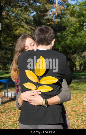 Loving couple hugging dans le parc tout en maintenant les feuilles d'automne jaune Banque D'Images