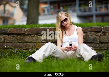 Jeune femme assise avec son téléphone cellulaire dans un parc Banque D'Images