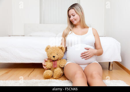 Jeune femme enceinte assise sur le sol à côté d'un ours en peluche Banque D'Images