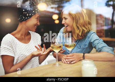 Deux jolies bénéficiant d''un verre de vin blanc ensemble dans un pub, assis à une table de rire et de bavarder avec des réflexions Banque D'Images