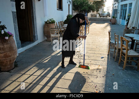 Une femme âgée travaille dans la lumière du matin, nettoyage de la place du village d'Anogia sur l'île de Crète en Grèce Banque D'Images