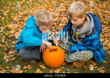 Les enfants de mêmes parents de garçons blonds hollowing out halloween citrouille à l'extérieur dans le jardin, assis sur la pelouse d'herbe d'automne, Banque D'Images