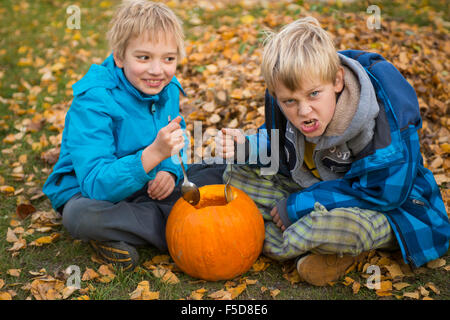 Les enfants de mêmes parents de garçons blonds hollowing out halloween citrouille à l'extérieur dans le jardin, assis sur la pelouse d'herbe d'automne, Banque D'Images