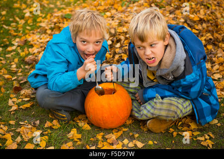 Les enfants de mêmes parents de garçons blonds hollowing out halloween citrouille à l'extérieur dans le jardin, assis sur la pelouse d'herbe d'automne, Banque D'Images