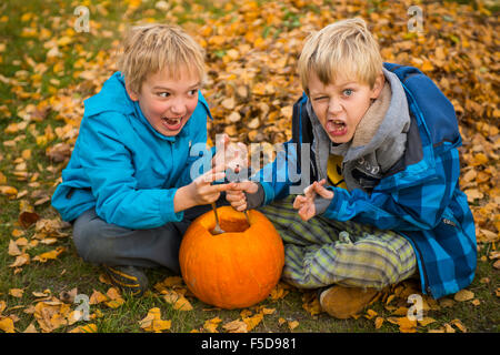 Les enfants de mêmes parents de garçons blonds hollowing out halloween citrouille à l'extérieur dans le jardin, assis sur la pelouse d'herbe d'automne, Banque D'Images