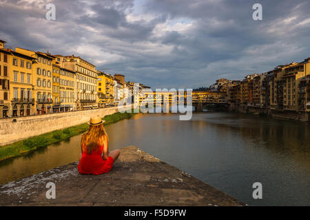 Une jeune femme en profitant de la vue sur le Ponte Vecchio et l'Arno par le coucher du soleil, Florence, Toscane, Italie. Banque D'Images