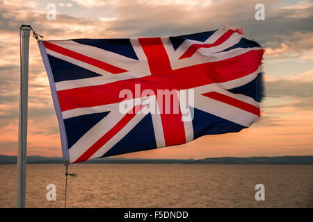 Une Union Jack voler contre un coucher de soleil sur la mer Banque D'Images