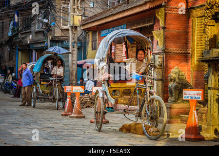 Népalais traditionnel rickshaw stationné sur la rue avec un coin couchage conducteur et son chien. Banque D'Images