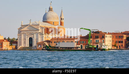 Un ferry transportant un camion et grue/digger en passant l'île de la Giudecca et Chiesa del Santissimo Redentore Venise Italie au crépuscule Banque D'Images