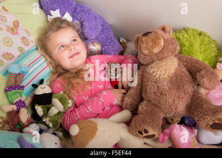 Girl lying on bed, entouré de peluches Banque D'Images