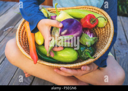 Boy sitting cross legged avec un panier de légumes Banque D'Images