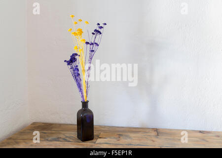 Violet et jaune fleurs séchées dans un vase bouteille bleu sur une vieille table en bois Banque D'Images