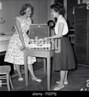 Historique Années 1950 Photo de deux jeunes filles adultes vêtus de vêtements la de l'époque, excité à la lecture d'un CD ou d'un disque vinyle sur un petit disque portable. Banque D'Images