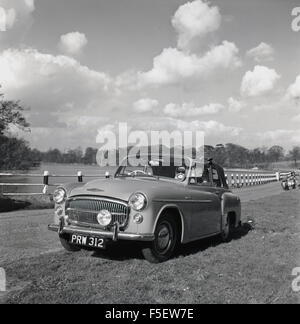 Historique années 1950, moteur voiture garée sur la route à côté herbeux. Banque D'Images