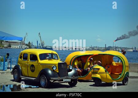 Des taxis et coco cubain jaune vintage cab stationnée sur le bord de l'eau à La Havane Cuba avec cheminée industrielle fumeurs à travers l'eau Banque D'Images