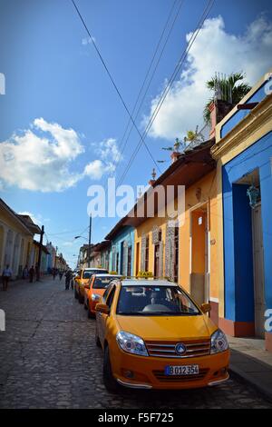 Les taxis jaune garée dans une ligne dans une rue pavée avec des maisons colorées à Trinidad Cuba Banque D'Images