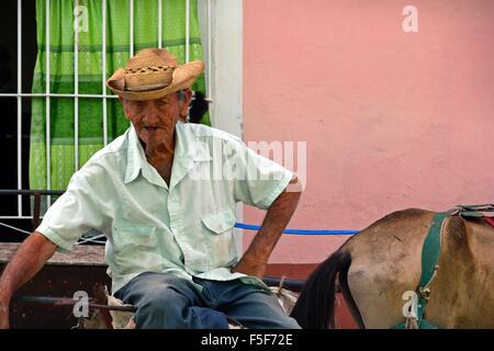 Vieux homme assis avec un cigare cubain et son cheval et panier à Trinidad Cuba à regarder l'appareil photo Banque D'Images