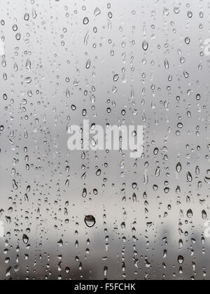 Après de fortes pluies, de nombreuses gouttes de pluie sont dégoulinant le long d'une fenêtre. Silhouette diffuse d'une ville émerge à l'arrière. Banque D'Images