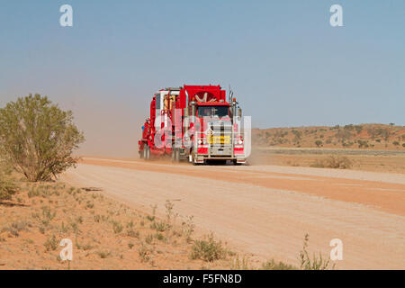 Road train, semi-remorque rouge énorme / camion chargé de l'équipement minier avant de nuage de poussière sur la route de l'outback australien Banque D'Images