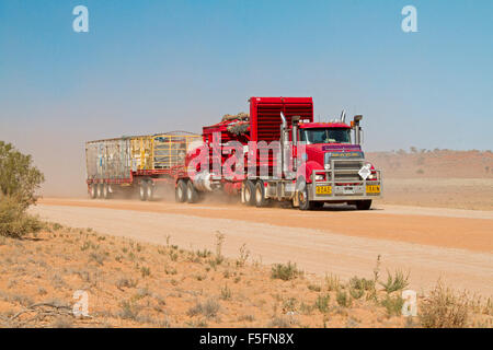 Road train, semi-remorque rouge énorme / camion chargé de l'équipement minier avant de nuage de poussière sur la route de l'outback australien Banque D'Images