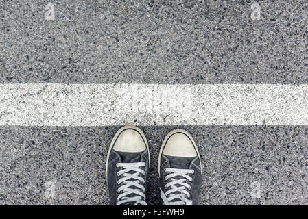 Homme debout à la frontière sur la chaussée urbaine, vue de dessus de pieds de jeunes hommes portant des chaussures de sport, en attente derrière la ligne Banque D'Images