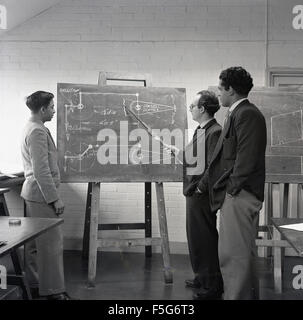 Histoire des années 1950, deux jeunes hommes apprentis ingénieurs ou étudiants dans une salle de classe debout sur un tableau noir avec un instructeur ou un enseignant qui enseigne la géométrie, Angleterre, Royaume-Uni. Banque D'Images