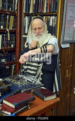 Un vieux juif religieux man putting sur phylactères tefillin au matin contre une synagogue de Brooklyn, New York. Banque D'Images