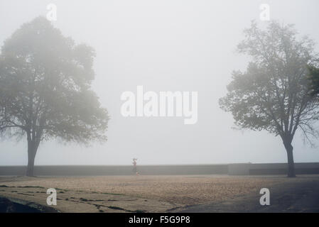 Lone jogger sur la rive du fleuve sur misty froid matin d'automne Banque D'Images