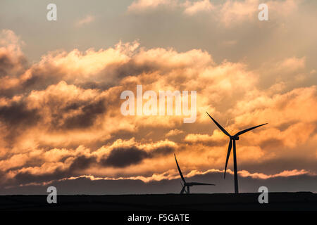 Nuageux ciel dramatique d'or au coucher du soleil avec deux éoliennes qui se profile à l'avant-plan Banque D'Images