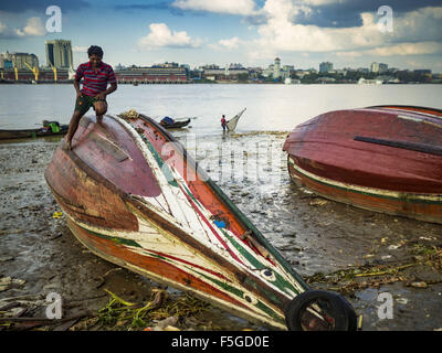 4 novembre 2015 - Dala, Division de Yangon, Myanmar - Un ouvrier répare la coque d'un petit traversier en bois sur les rives de la rivière Yangon Yangon de Dala, est dans l'arrière-plan. Dala est situé sur la rive sud du fleuve Yangon en face du centre-ville de Yangon, Myanmar. De nombreux Birmans vivent dans Dala et les communautés environnantes et aller de l'autre côté de la rivière dans le centre de Yangon pour travailler. Avant la Seconde Guerre mondiale, l'Irrawaddy Flotilla Company avait ses principaux chantiers de Dala. Cette tradition perdure dans les petites entreprises les travaux de réparation sur les centaines de petits bateaux en bois qui servent de ferries de banlieue pour les gens o Banque D'Images