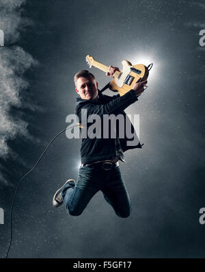 Guitariste de Rock and Roll jumping de guitare électrique avec de la fumée et de la poudre en arrière-plan Banque D'Images
