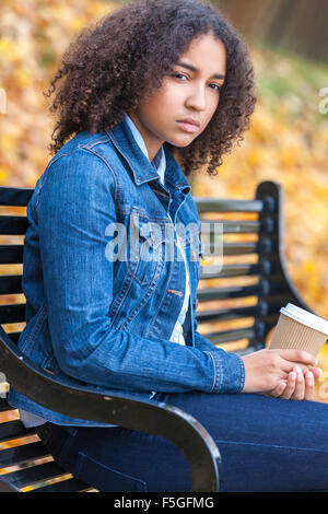 Réfléchis bien triste ou déprimé mixed race African American girl adolescent femme jeune femme à boire le café à emporter dans la région de park Banque D'Images