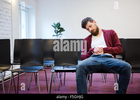 Jeune homme à la barbe en brun et bleu jeans sweat à s'endormir à la salle de conférence Banque D'Images