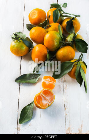 Un tas de mandarines juteuses avec des feuilles vertes sur un fond de bois blanc Banque D'Images