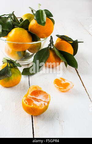 Mandarines mûres avec des feuilles dans un bol en verre sur un fond de bois blanc vertical mise au point sélective Banque D'Images