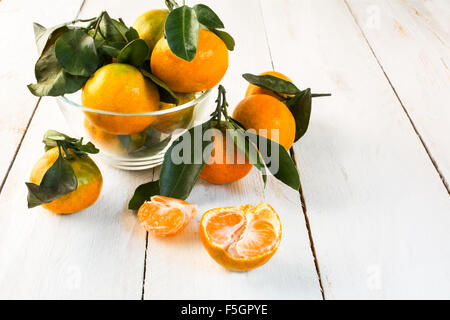 Mandarines mûres avec des feuilles vertes dans un bol en verre sur un fond de bois blanc l'horizontale Banque D'Images